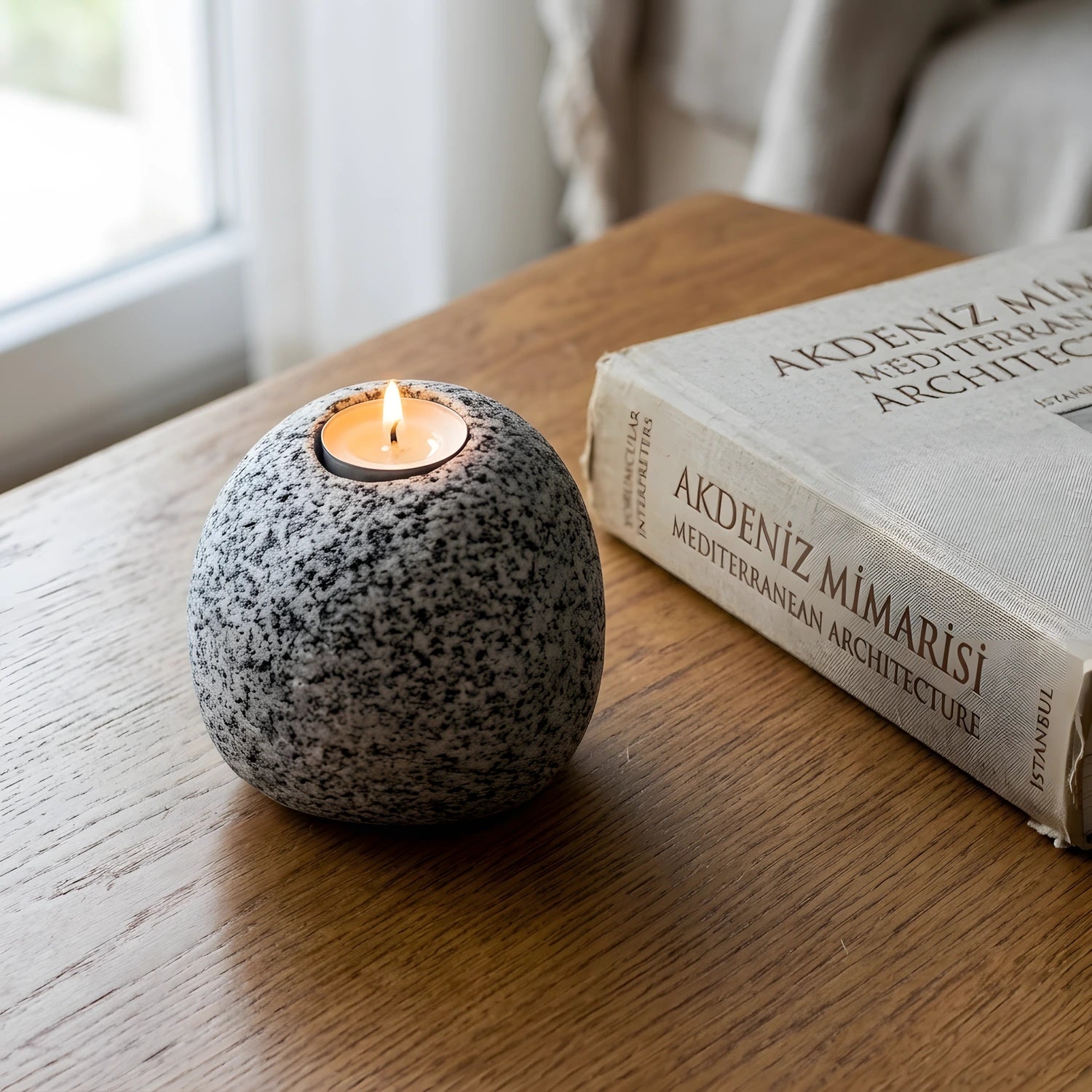 Ahşap masa üzerinde kitapların yanında duran yanan Bergama graniti tealight mumluk.