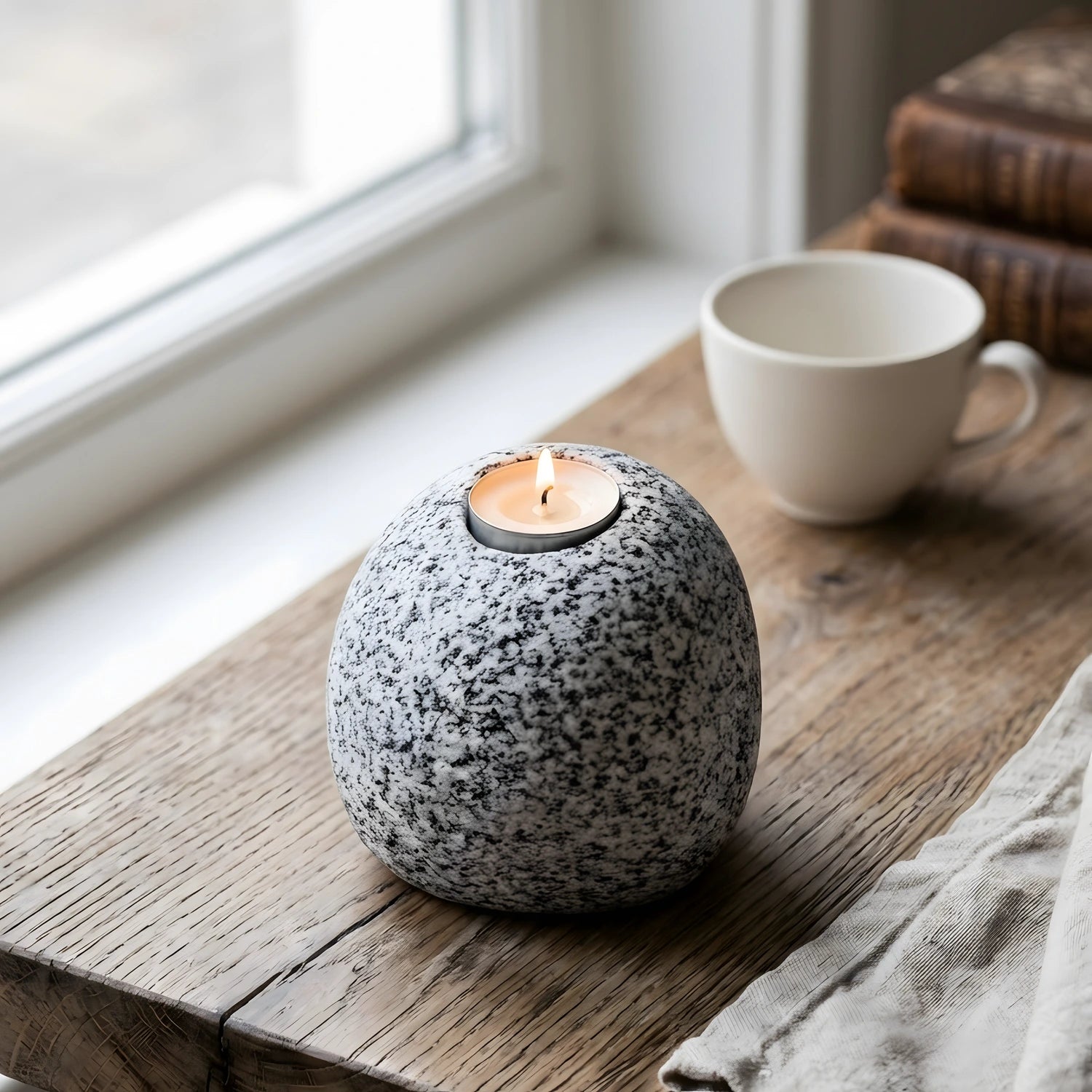 Pencere kenarındaki rustik ahşap pervaz üzerinde duran yanan Bergama graniti tealight mumluk.