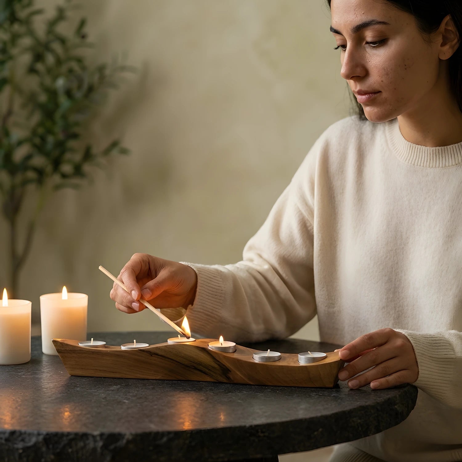 Loş ışıklı modern bir odada ahşap mumluğun tealight mumlarını yakan kadın.