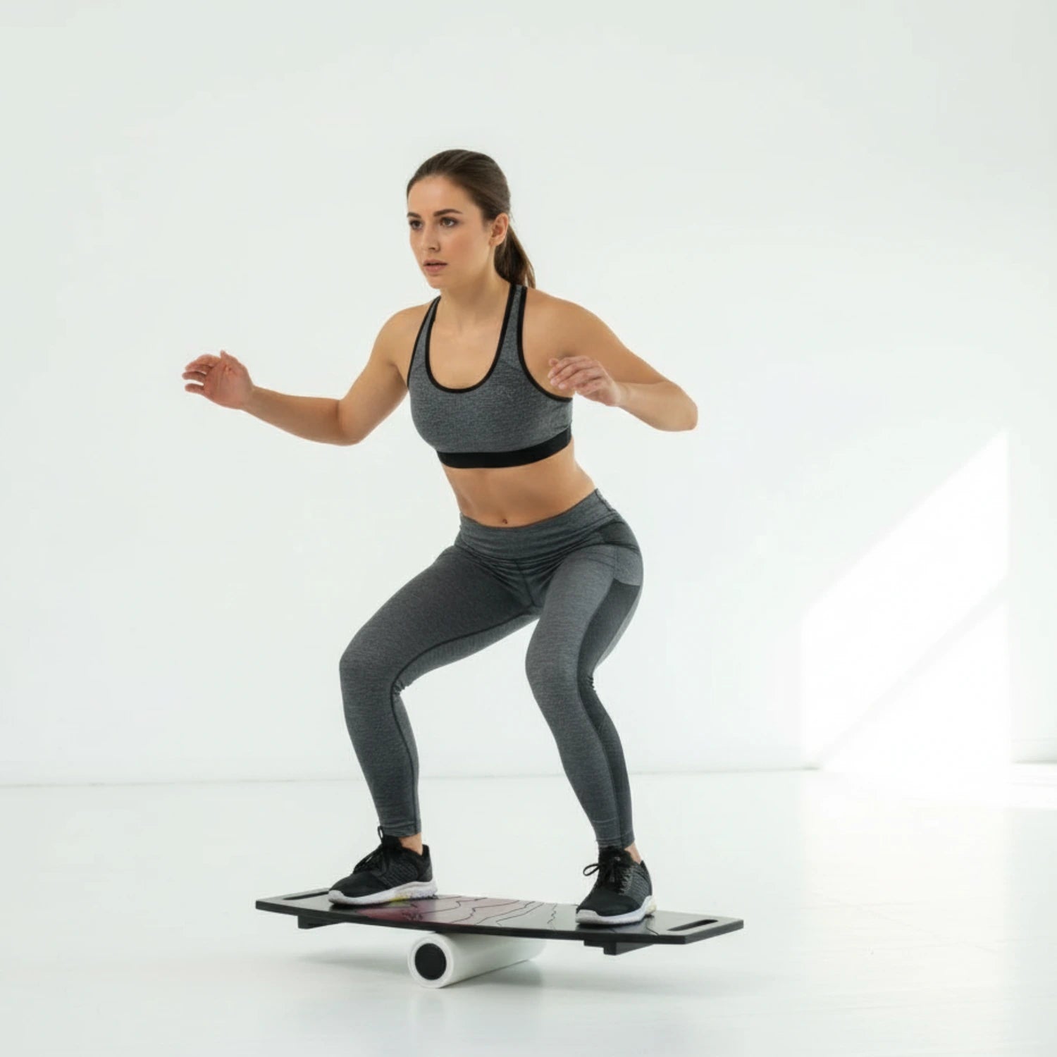 Denge tahtası üzerinde squat hareketi yaparak alt vücut çalışan kadın fitness sporcusu.