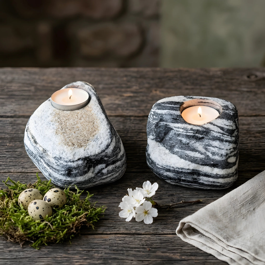 Ahşap masa üzerinde Paskalya dekoru (yosun, yumurtalar, çiçekler) ile birlikte sergilenen iki adet siyah ve beyaz çizgili doğal taş tealight mumluk.