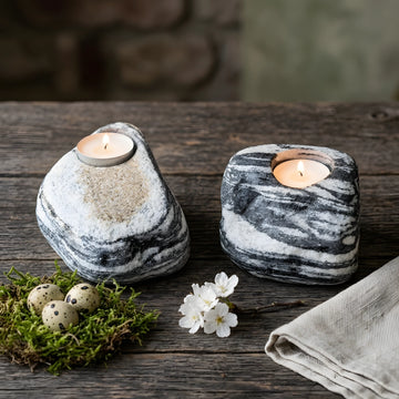 Ahşap masa üzerinde Paskalya dekoru (yosun, yumurtalar, çiçekler) ile birlikte sergilenen iki adet siyah ve beyaz çizgili doğal taş tealight mumluk.